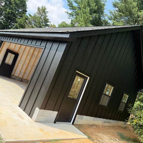 The side of the finished black board-and-batten garage, with the entry door and three windows installed and trimmed