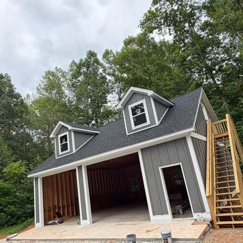 A finished two-storey detached garage with gray board-and-batten siding, white trim, two dormer windows and an exterior wood staircase